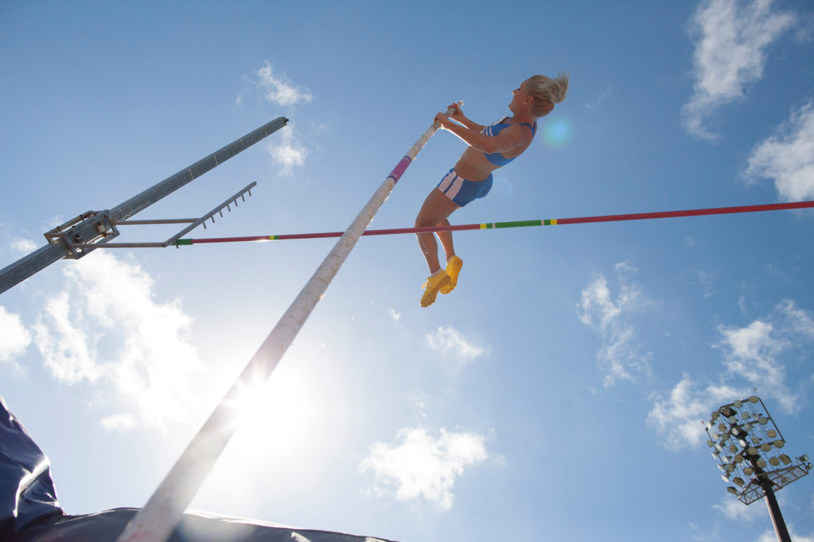 Female track and field athlete pole vaulting under sunny sky